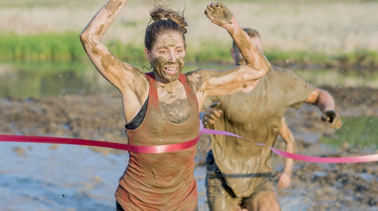 Muddy women running across red finish line
