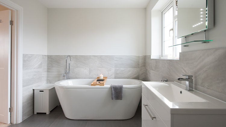 Clean bathroom with grey tiles and a white tub 