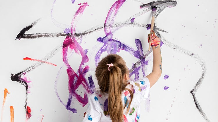 Child painting bright colors on a white wall