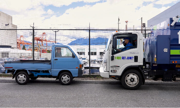 A daihatsu mini truck and 1-800-GOT-JUNK? truck parked on the street. 