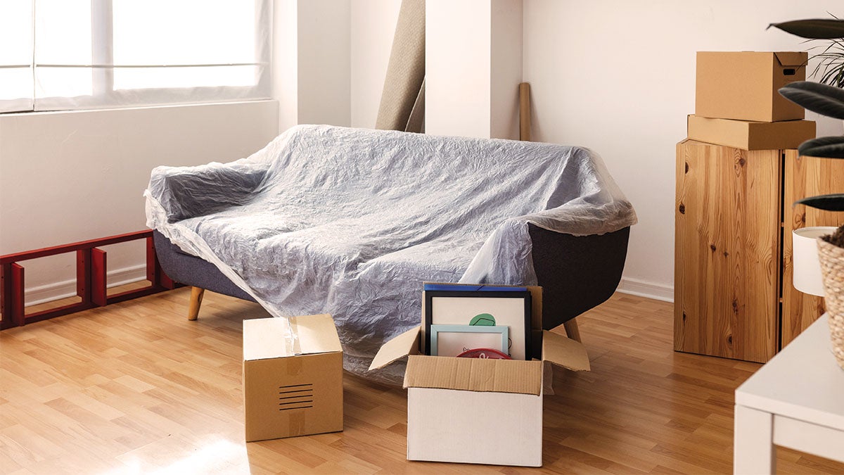 A couch with a mocing cover on it and moving boxes around it
