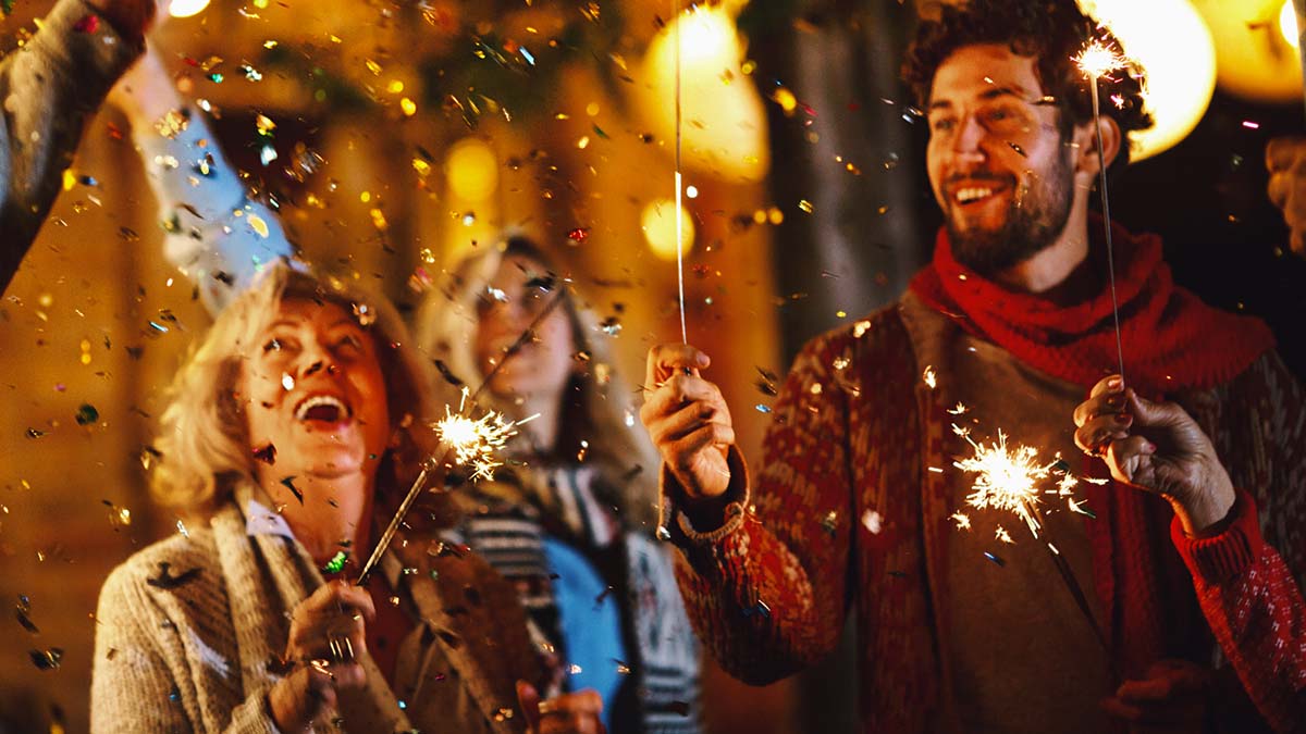 Group photo of two women and a man cheering at New Years Eve and holding sparklers