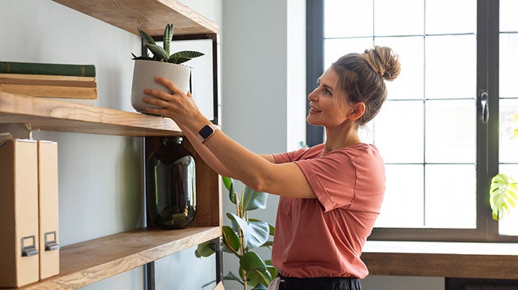 Woman placing a decorative planter on top of a shelf in a living room space
