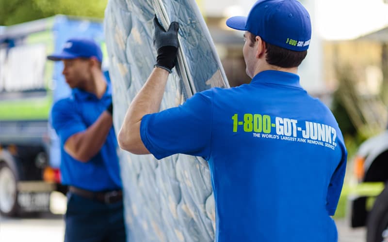 Two 1-800-GOT-JUNK? team members carrying a mattress for recycling