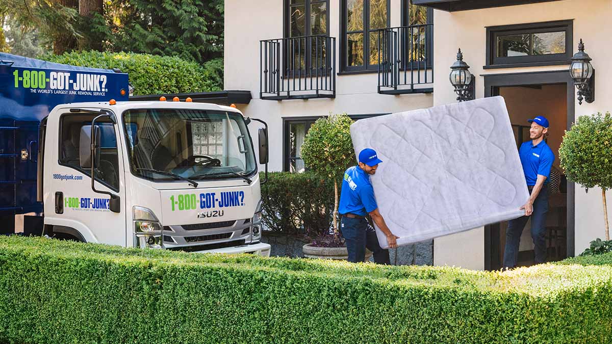 Two 1-800-GOT-JUNK? team mebers carrying a large mattress out of a house.