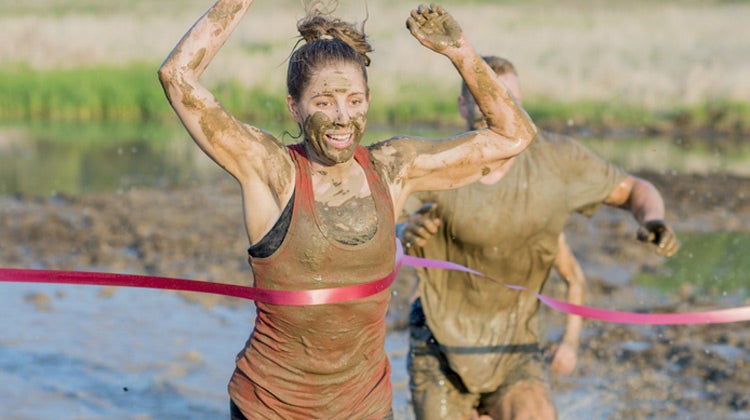 Muddy women running across red finish line Muddy women running across red finish line