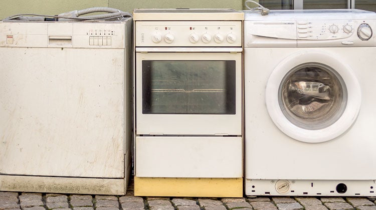 Three old and dirty appliances sitting outside of a building