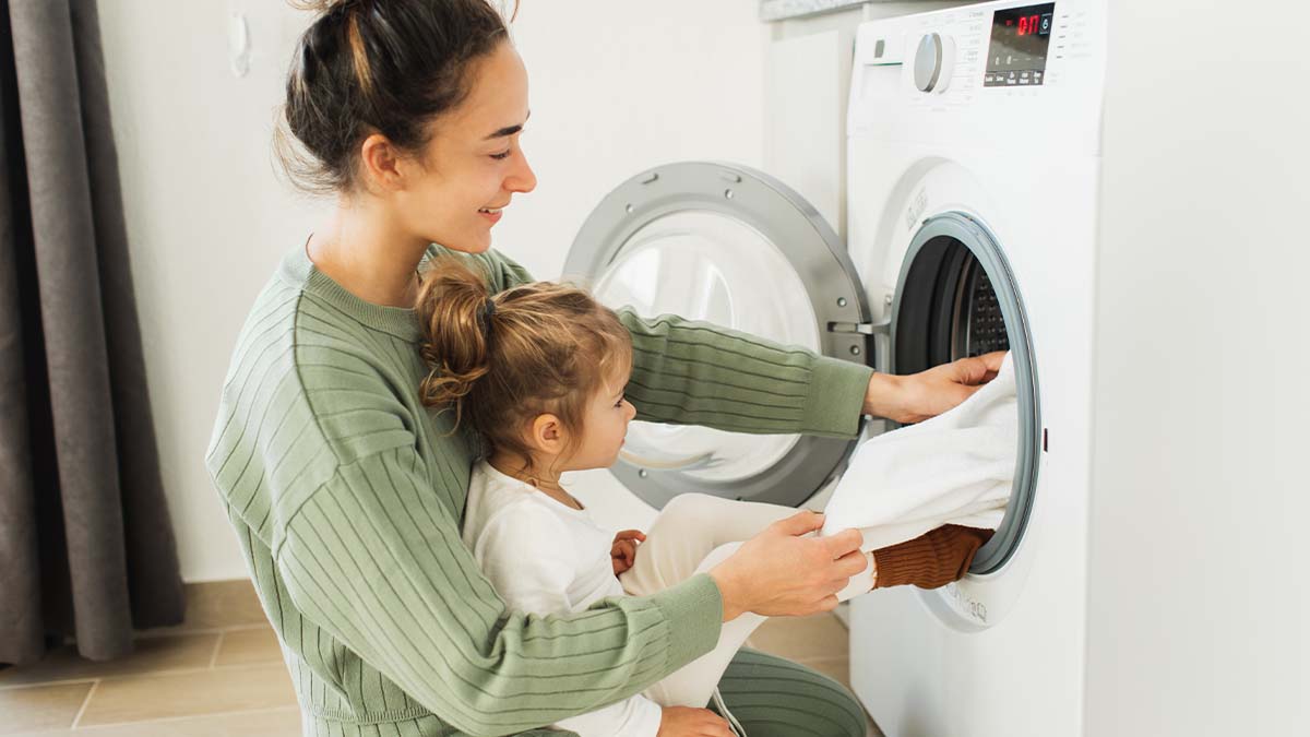 Mother and young daughter taking white sheets out of drying machine