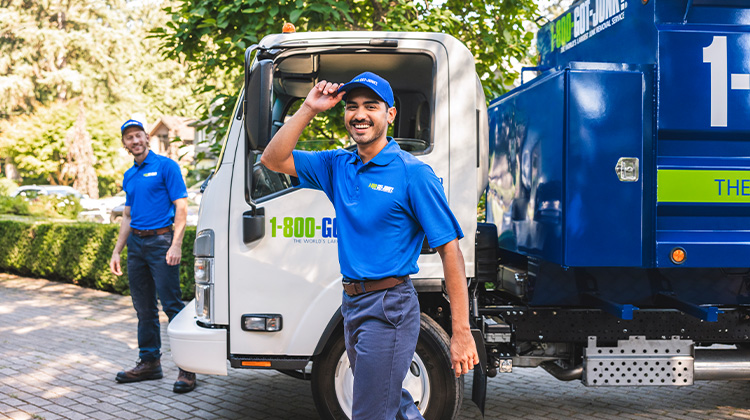 Two truck team members standing smiling in front of a 1-800-GOT-JUNK? truck.