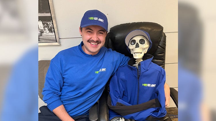 1-800-GOT-JUNK? team member smiling next to a skeleton decoration wearing a 1-800-GOT-JUNK? jacket