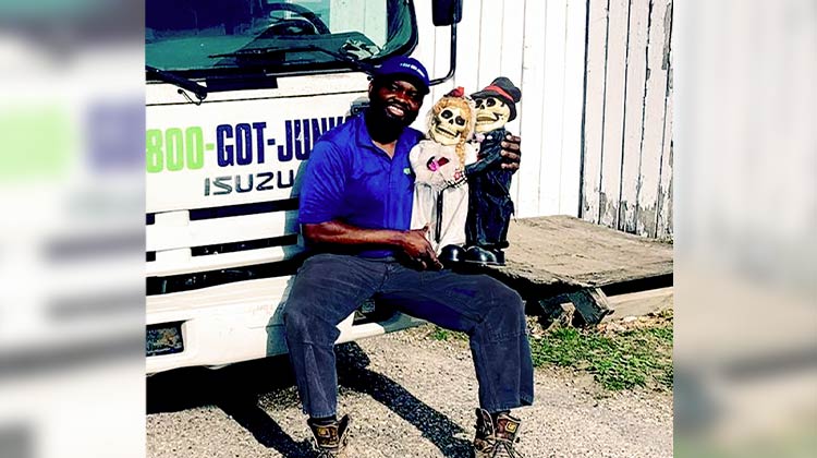 1-800-GOT-JUNK? team member holding two skeleton dolls wearing wedding attire