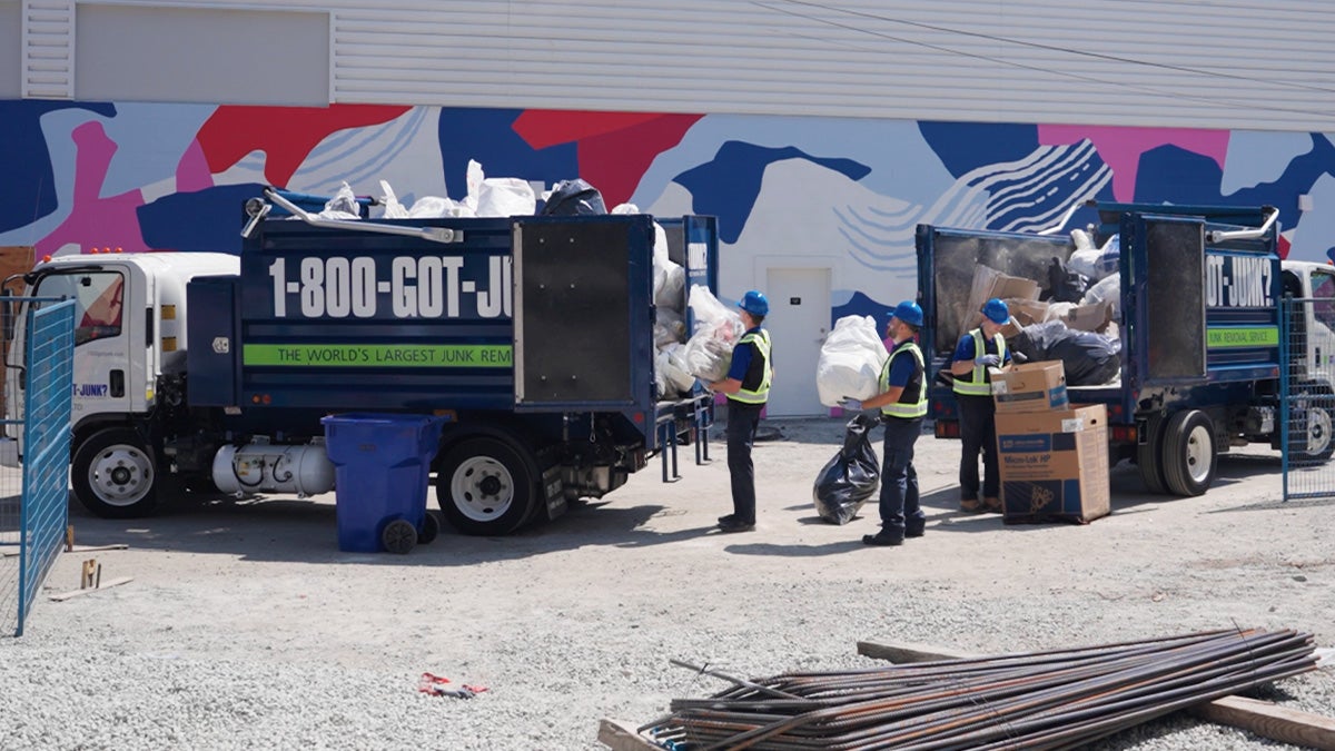 1-800-GOT-JUNK? truck team members loading waste bags filled with construction debris onto the truck bed.”
