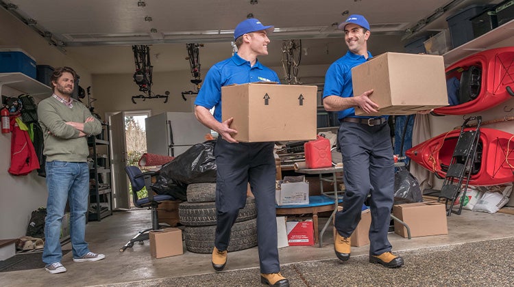 Two 1-800-GOT-JUNK? team members removing junk from a garage while customer watches Two 1-800-GOT-JUNK? team members removing junk from a garage while customer watches