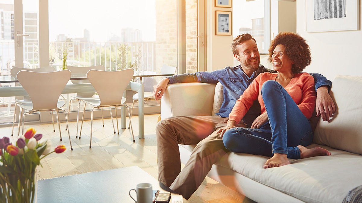 Couple sitting on couch in clean home with flowers on table