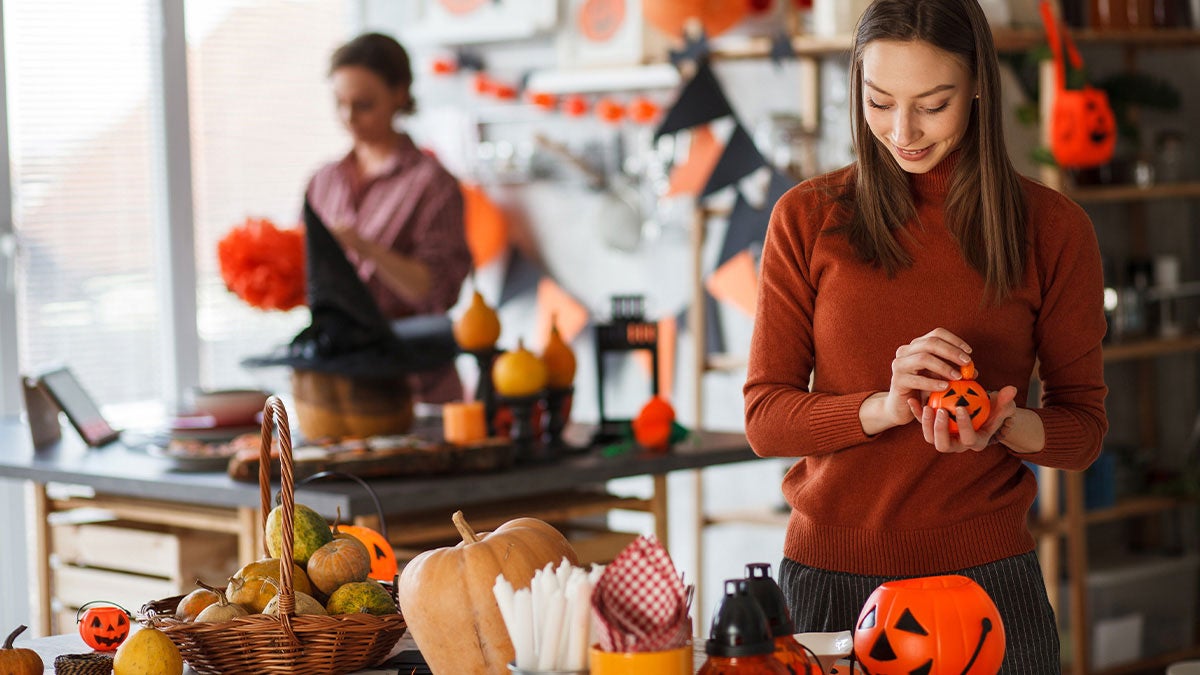 Woman holding small decorative pumpkin behind a crafting table