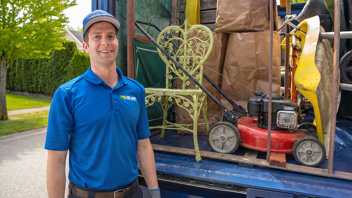 A 1-800-GOT-JUNK? Truck Team Member disposing a lawnmower into the back of a truck.