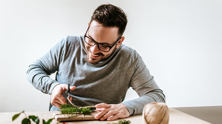 Man wrapping a present with recycled paper and greenery 