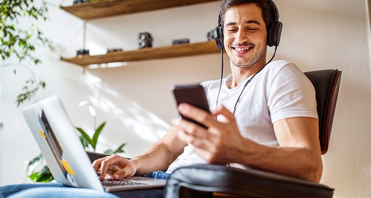 Man wearing headphones using a phone and computer Man wearing headphones using a phone and computer