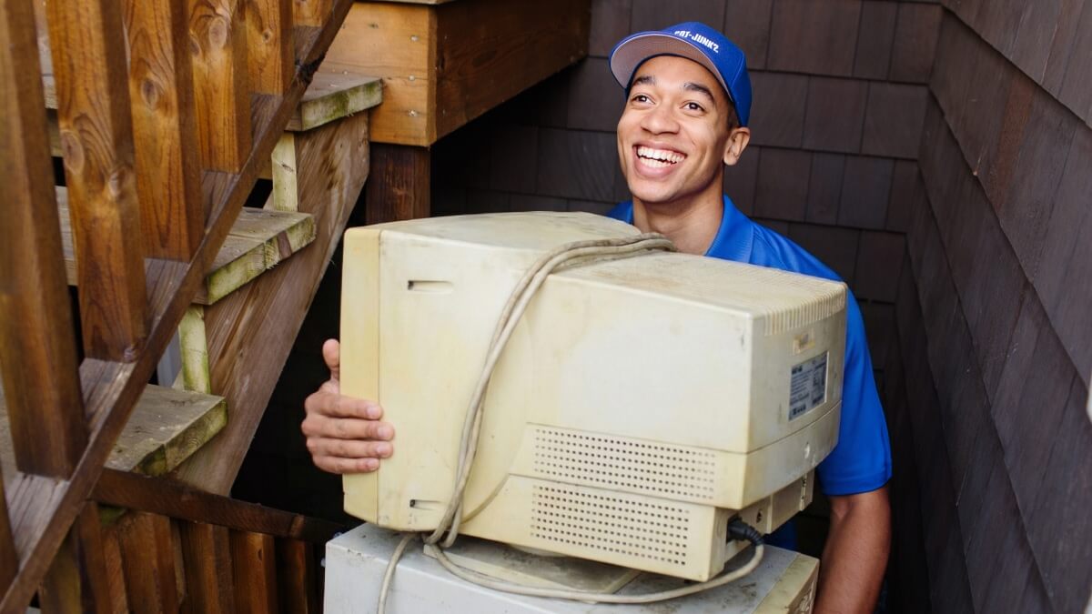 A 1-800-GOT-JUNK? team member smiling while carrying a large old computer monitor.