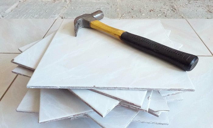 How to remove tile floor Hammer resting on a stack of old white floor tiles