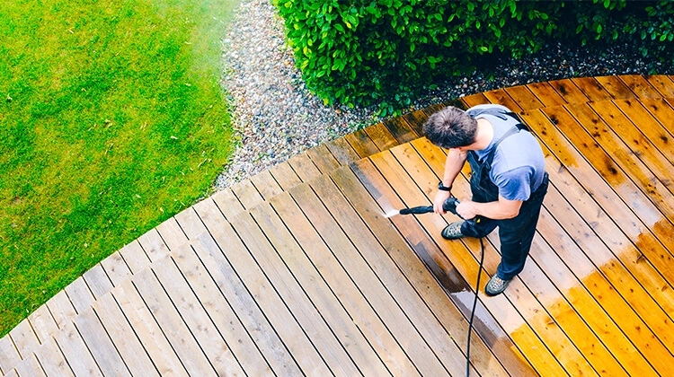Man in overalls power washing a wood deck