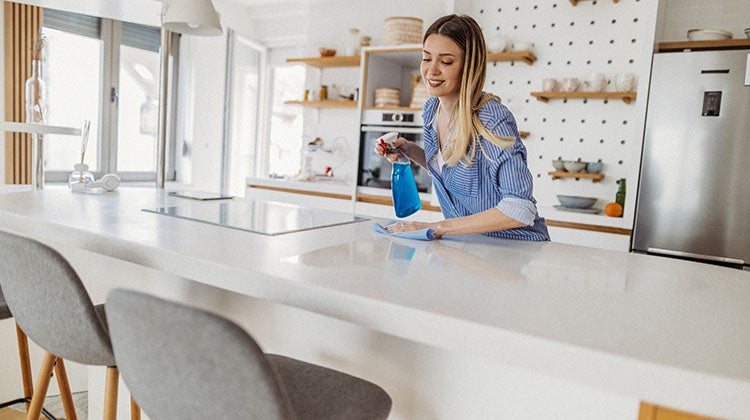 Woman cleaning kitchen counter with disinfectant spray and cloth