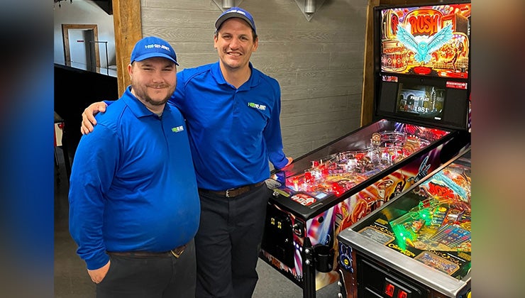 Two 1-800-GOT-JUNK? Team Members standing in front of pinball machines