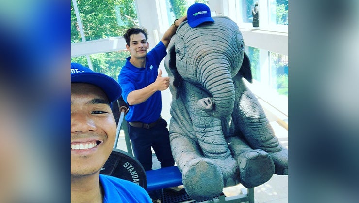 Two 1-800-GOT-JUNK? truck team members taking a selfie with an elephant statue wearing a 1-800-GOT-JUNK? hat