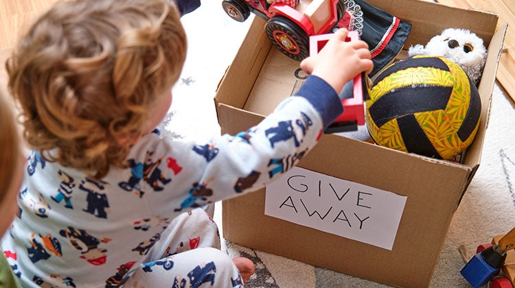 Young child putting toys in a box labelled "Give Away"