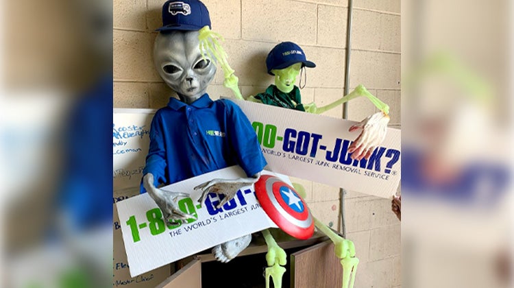 Grey alien and green skeleton decorations propped up with 1-800-GOT-JUNK? clothing and signs