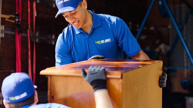 1-800-GOT-JUNK? Team member smiling while carefully carrying an old dresser