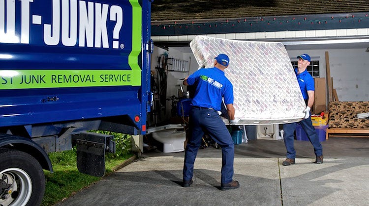 Two 1-800-GOT-JUNK? team members carrying an old mattress to the truck