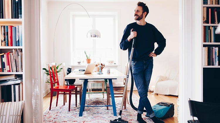 Man standing in living room with a vacuum, admiring his recently cleaned home