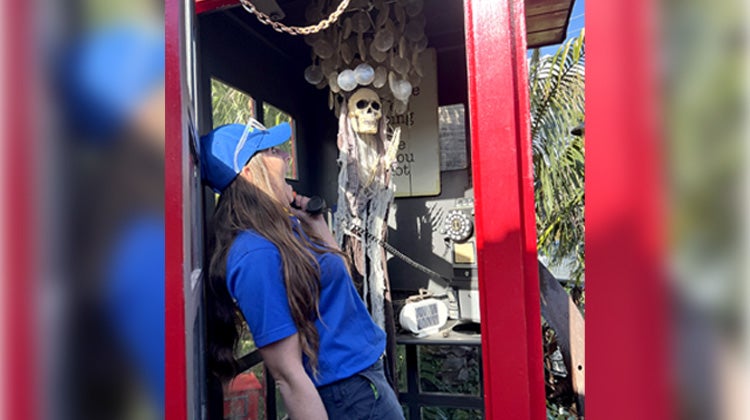 1-800-GOT-JUNK? Team member screaming in phone booth with a skull decoration inside