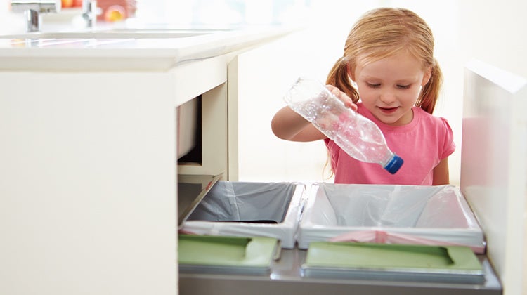 Young girl putting an empty bottle into the recycling under the sink 