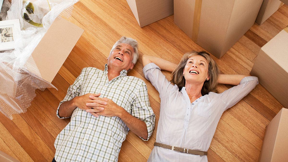 Husband and wife smiling, lying down on the floor surrounded by moving boxes