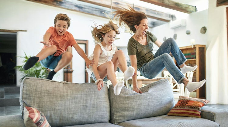 Mom and two kids jumping onto a couch 