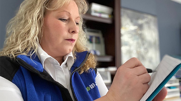 Pierrette wearing a 1-800-GOT-JUNK? vest while writing a list 