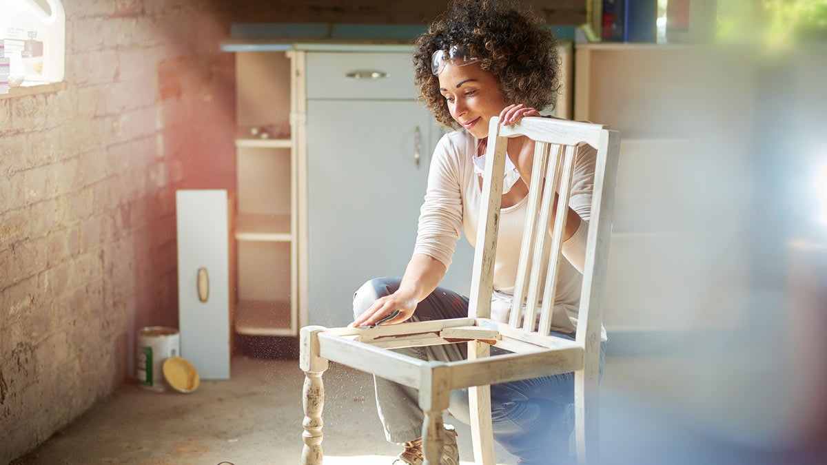 Women dusting wooden chair in storage room