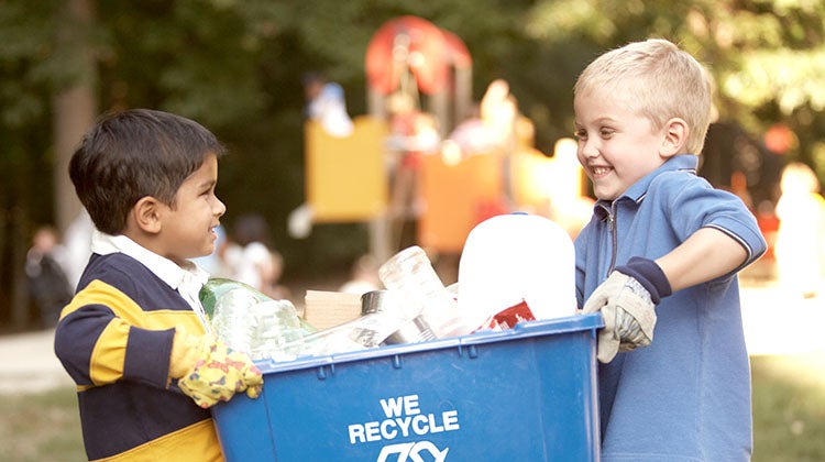 Two small children holding a full recycling bin