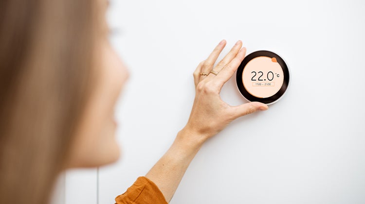Woman adjusting a wall mounted digital thermostat Woman adjusting a wall mounted digital thermostat