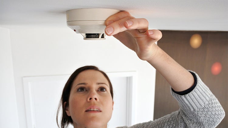Woman checking a smoke detector Woman checking a smoke detector