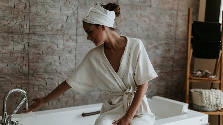 Woman in a robe turning on her bathtub 