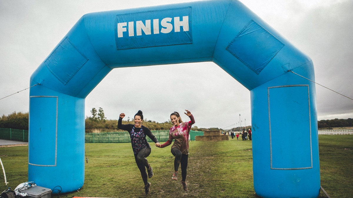 Two smiling runners crossing muddy finish line
