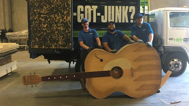 Large acoustic guitar in front of a 1-800-GOT-JUNK? truck 