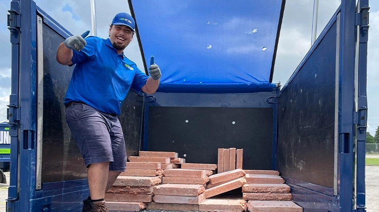 1-800-GOT-JUNK? team member smiling next to salmon bricks 1-800-GOT-JUNK? team member smiling next to salmon bricks